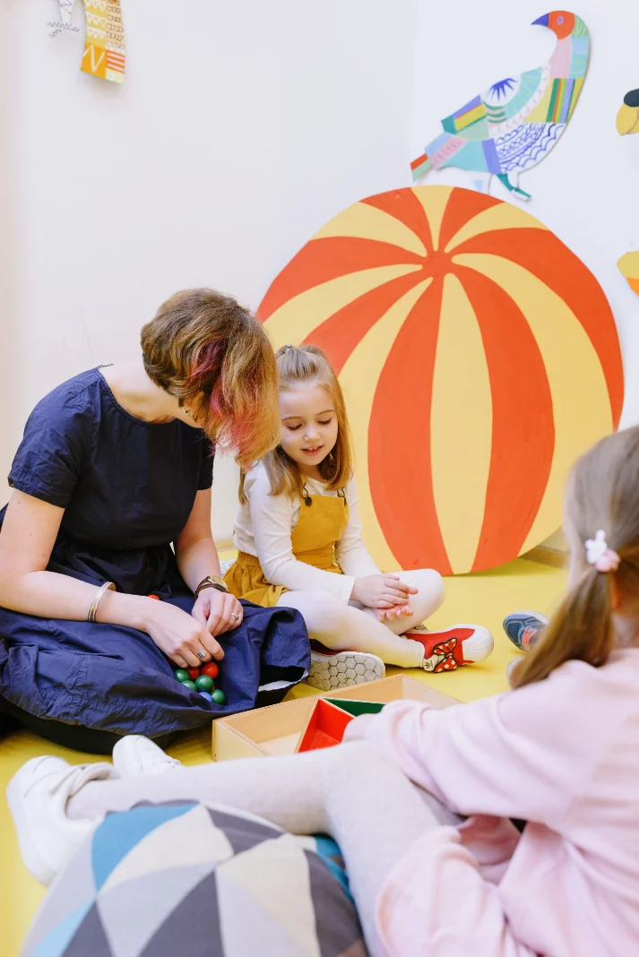Nauczycielka bawi się z dziewczynką na dywanie w kolorowej sali przedszkolnej